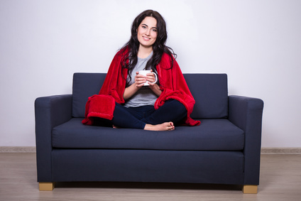 young woman sitting on sofa with mug of tea wrapped in red blank
